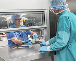 Sterile processing technician passes a medical instrument through the pass-through window to another technician