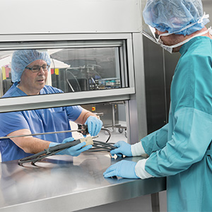 Sterile processing technician passes a medical instrument through the pass-through window to another technician