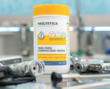 Container of PROLYSTICA Pass-Thru Disinfectant Wipes placed on a stainless steel surface, surrounded by surgical instrument components and connectors